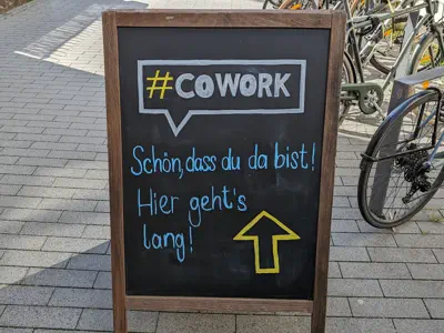Aufsteller mit Hinweis: #COWORK. Schön, dass du da bist. Hier geht's lang.