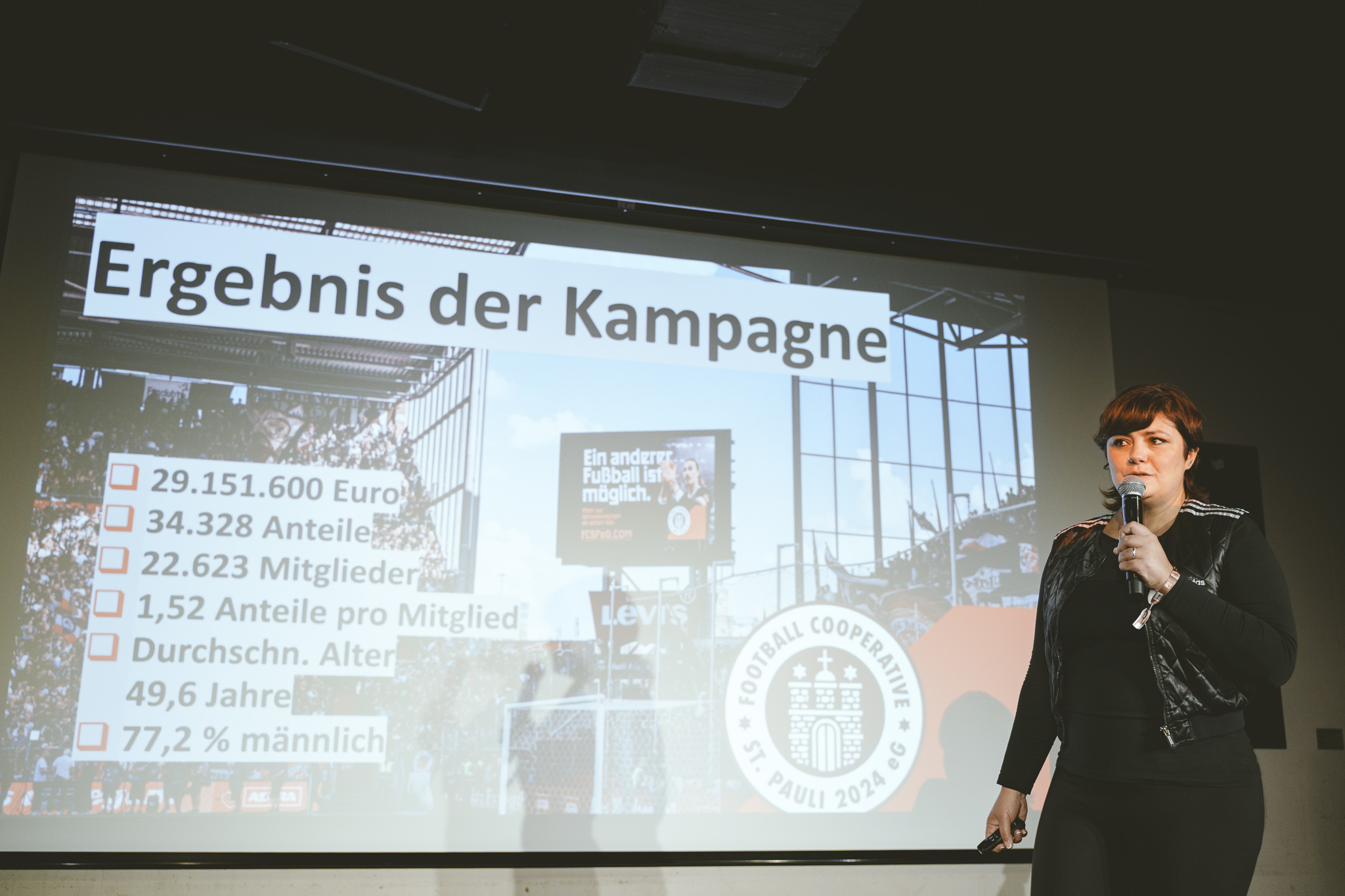 Eine Frau mit kurzen dunklen Haaren vor einer Präsentationsleinwand, auf der &ldquo;Ergebnis der Kampagne&rdquo; steht