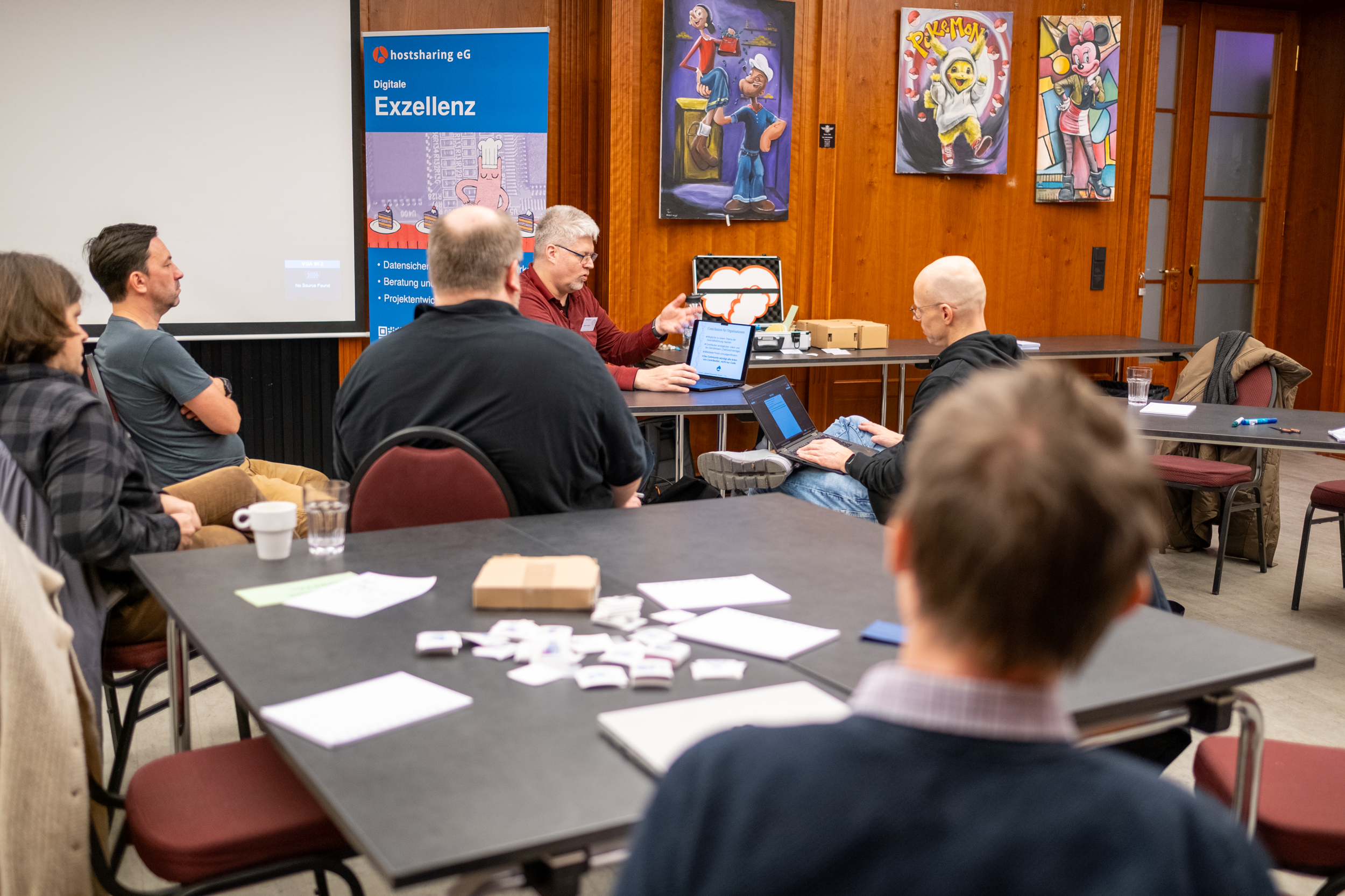 Die gleiche Situation aus anderem Blickwinkel. An den Holzwänden hängen Gemälde mit Comicfiguren