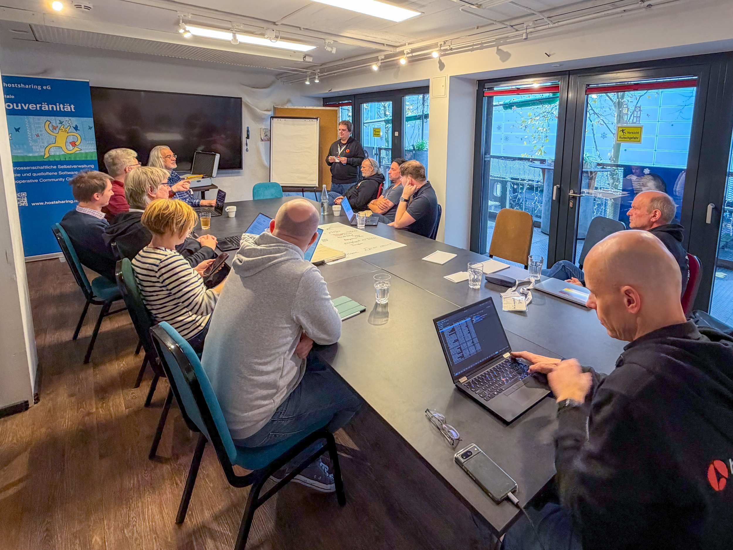Ein Dutzend Personen sitzt in einem Seminarraum. Eine Person steht neben einem Flipchart.