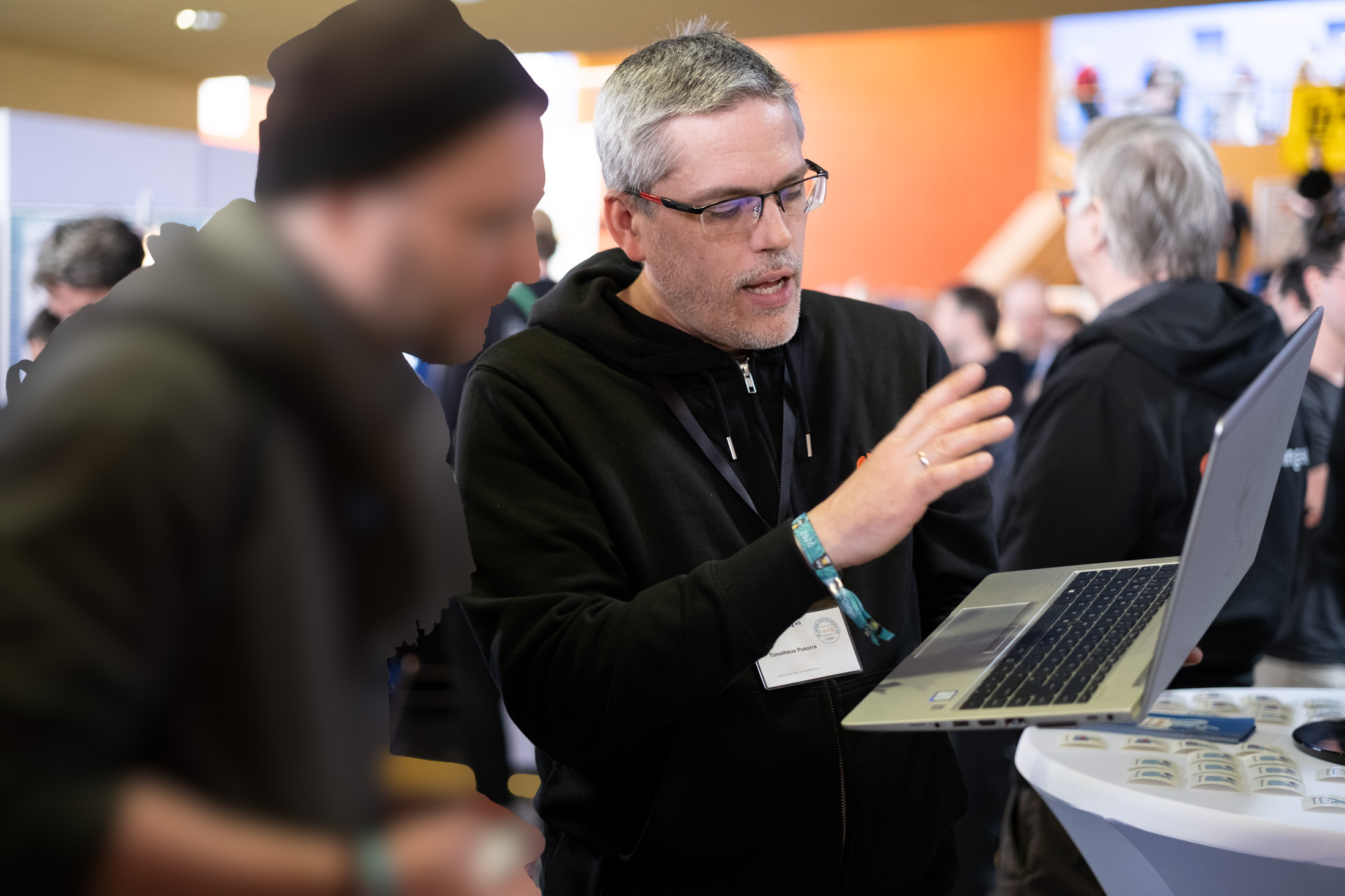 Ein Mitglied der Hostsharing eG hält ein Notebook in der Hand und erklärt einem Besucher etwas.