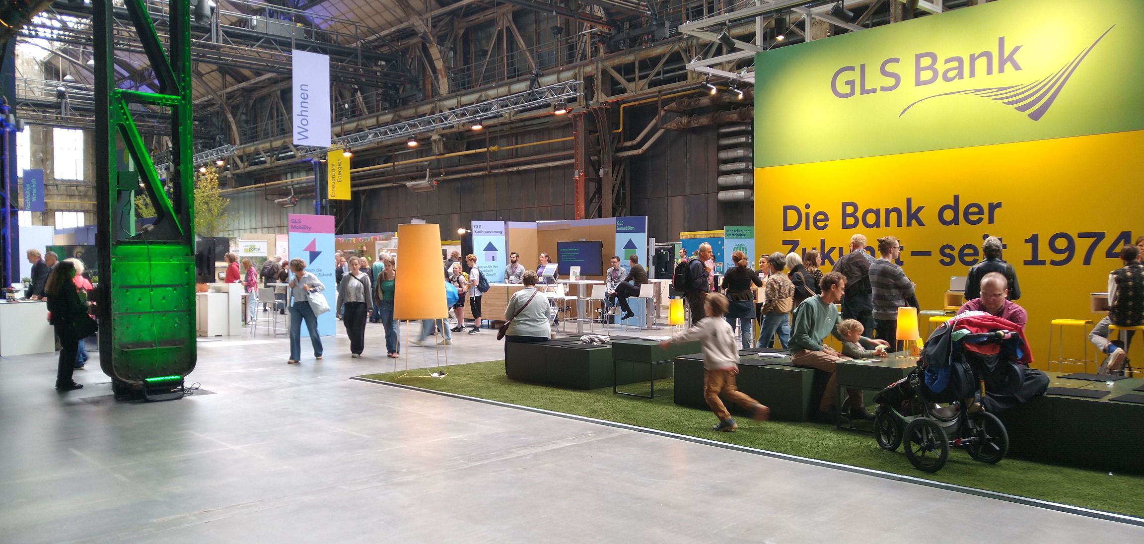 Historische Industriehalle. Man sieht Rohre an den Decken. Rechts der Stand der GLS Bank.