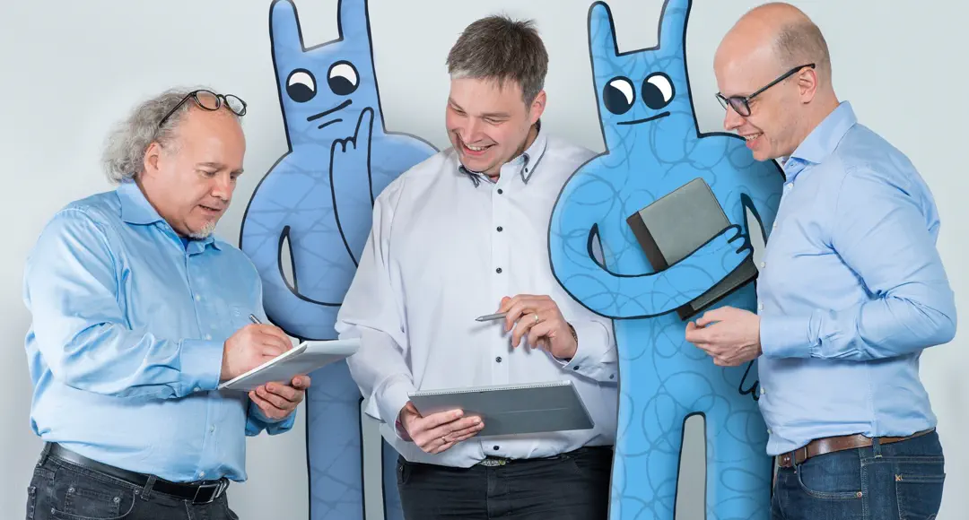 Drei Herren stehen mit zwei Hostsharing-Maskottchen zusammen und besprechen etwas.