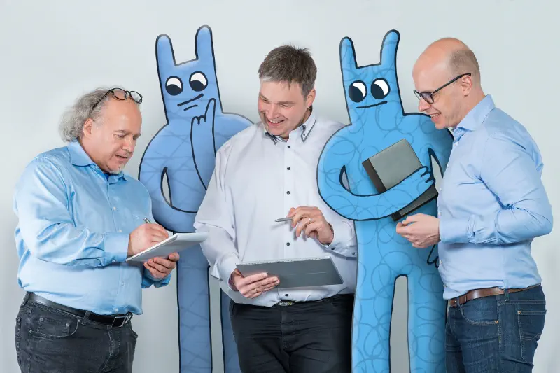 Drei Herren stehen mit zwei Hostsharing-Maskottchen zusammen und besprechen etwas.