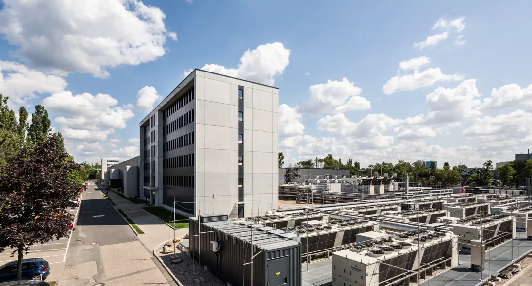 Industriegebäude, im Vordergrund Geräte, die aussehen wie Klimaanlagen. Blauer Himmel mit ein paar Wolken.