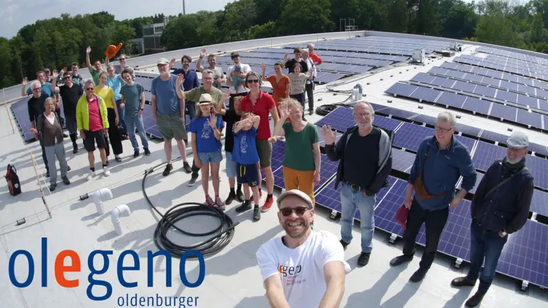 Menschen stehen auf einem Hausdach mit Photovoltaik und winken in die Kamera.