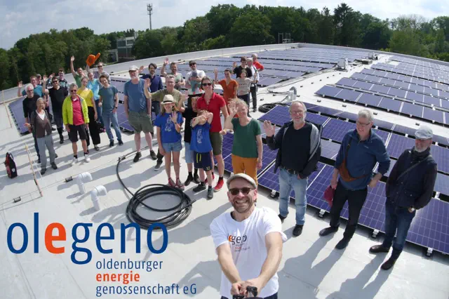 Menschen stehen auf einem Hausdach mit Photovoltaik und winken in die Kamera.