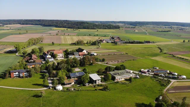 Luftbild einer Siedlung inmitten landwirtschaftlicher Flächen und Wälder.