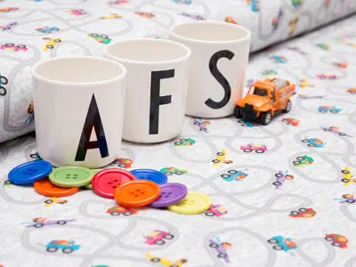 3 Tassen mit den Buchstaben A, F, S stehen auf Stoffballen, ein Spielzeugauto und bunte Knöpfe.