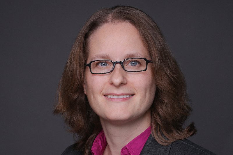 Eine Frau mit dunkelblonden Haaren und eckiger Brille lächelt in die Kamera.