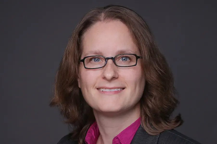 Eine Frau mit dunkelblonden Haaren und eckiger Brille lächelt in die Kamera.