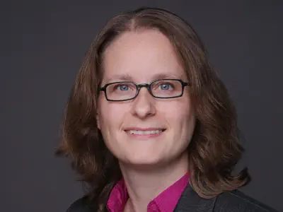 Eine Frau mit dunkelblonden Haaren und eckiger Brille lächelt in die Kamera.