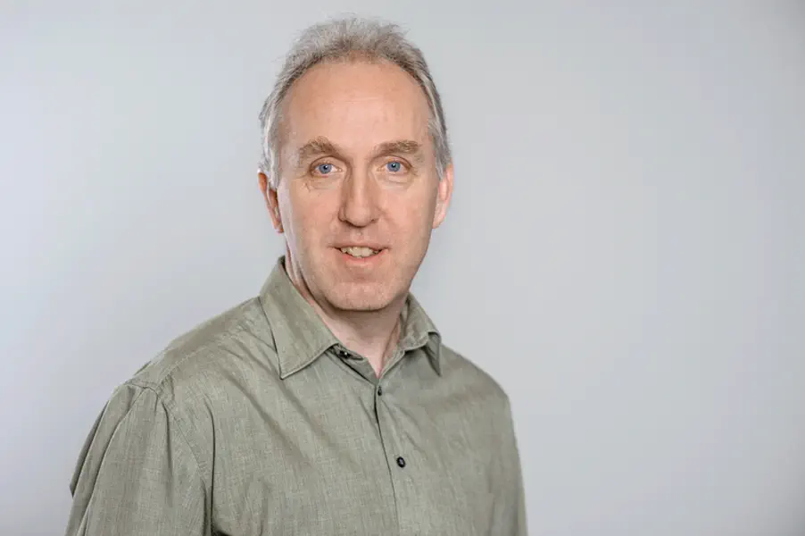 Ein Mann mit buschigen Augenbrauen schaut freundlich in die Kamera. Er trägt ein olivgrünes Hemd.