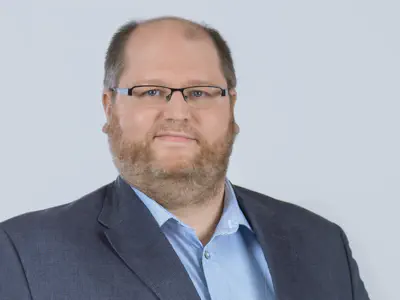 Freundlicher Mann mit graublondem Bart, hellblauem Hemd und dunkelblauem Sakko.