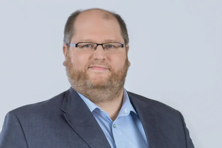 Freundlicher Mann mit graublondem Bart, hellblauem Hemd und dunkelblauem Sakko.