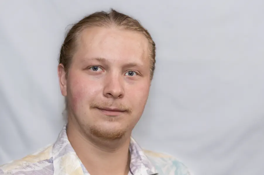 Sympathischer junger Mann mit zurückgekämmtem Haar und Bartansatz. Er träge ein legeres Hemd.