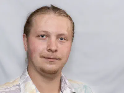 Sympathischer junger Mann mit zurückgekämmtem Haar und Bartansatz. Er träge ein legeres Hemd.