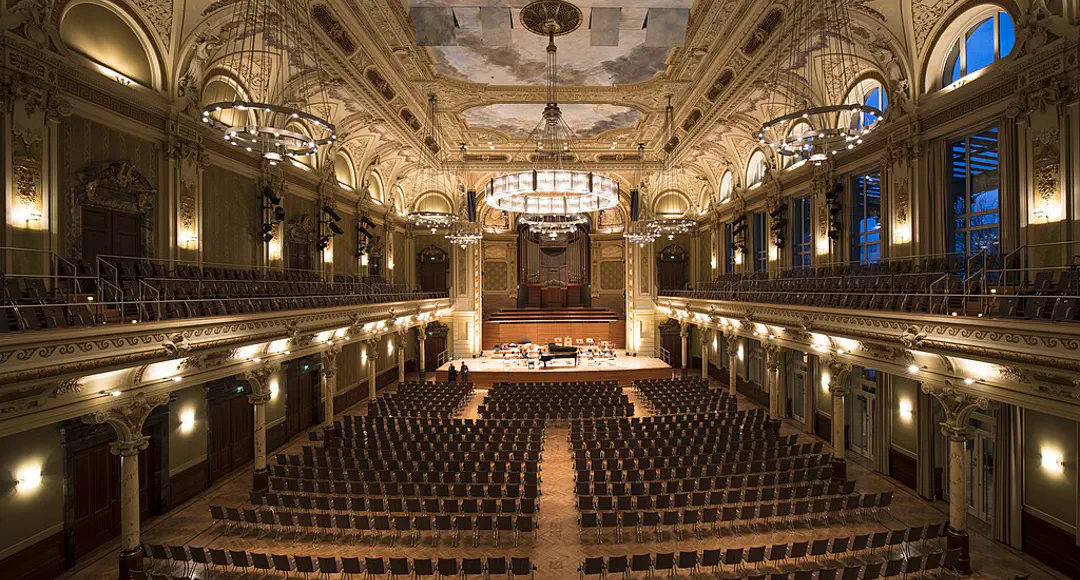 Großer menschenleerer Konzertsaal im Stil der Neorenaissance. Auf der Bühne ein Flügel.